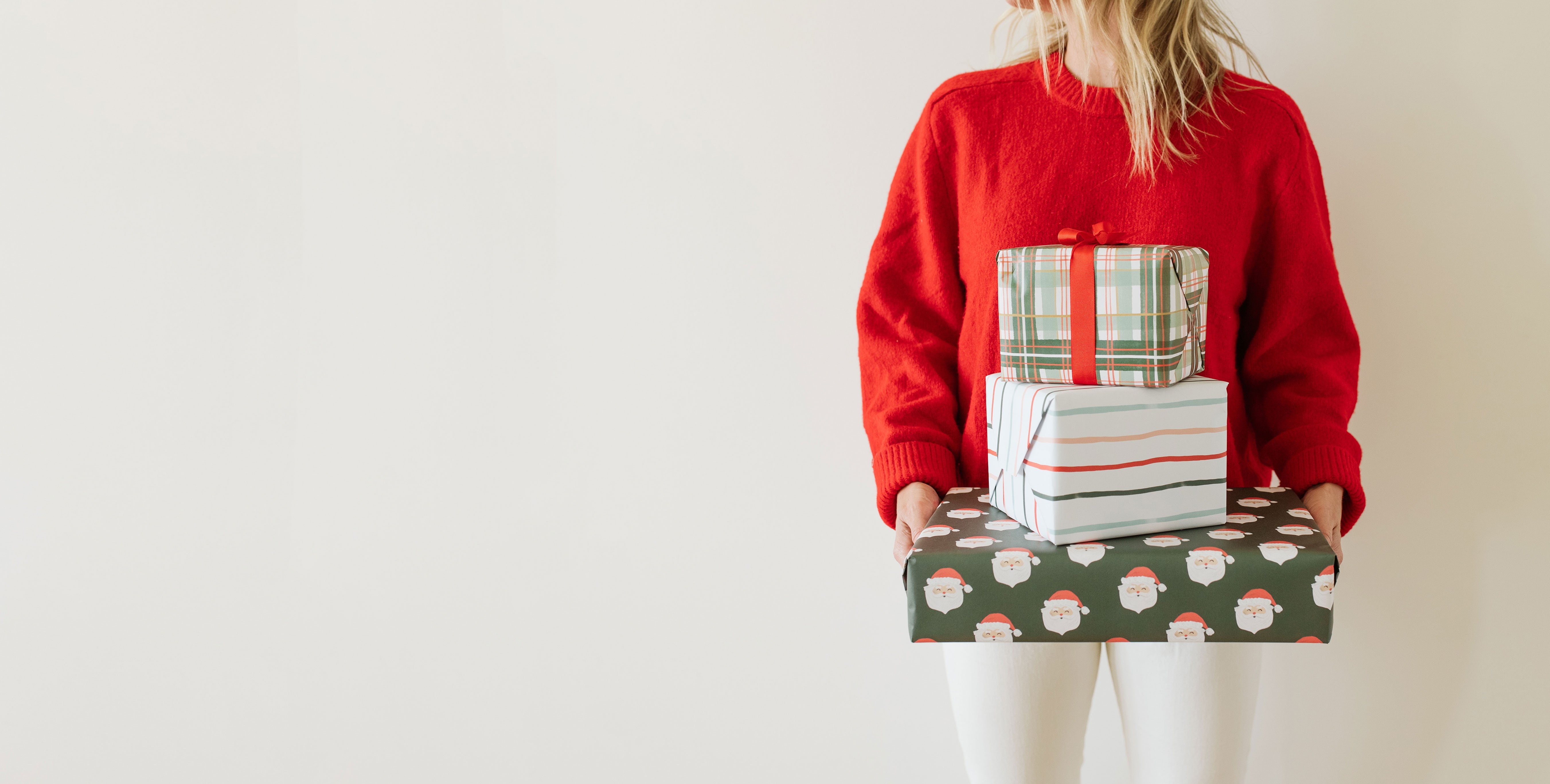 Person wearing a red sweater holding wrapped gifts by Ramona & Ruth against a plain background